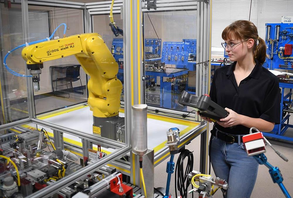 A student operates a robot in the industrial automation classroom on the Ayers campus